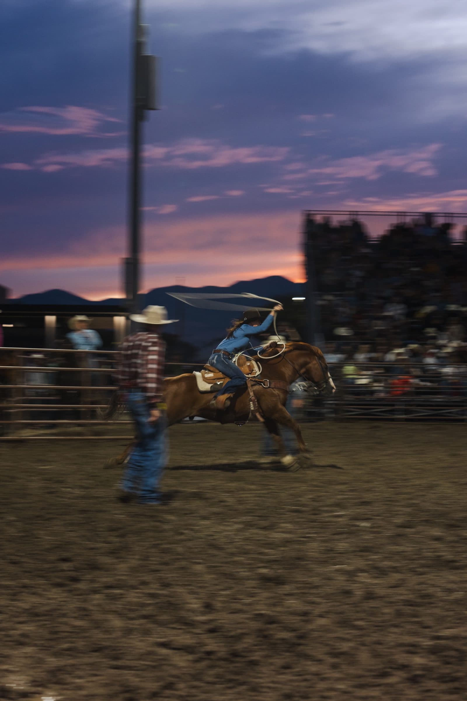 A bronc rider works against a pink dusk sky over the mountains